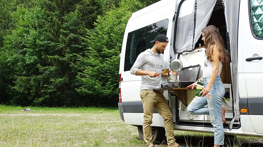 husband and wife cooking next to their bus