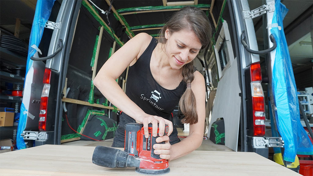 A woman sands a wooden board