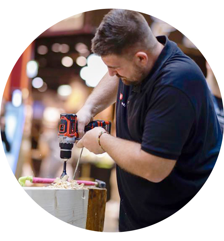 A man drilling a hole into a piece of wood with an Einhell cordless drill.