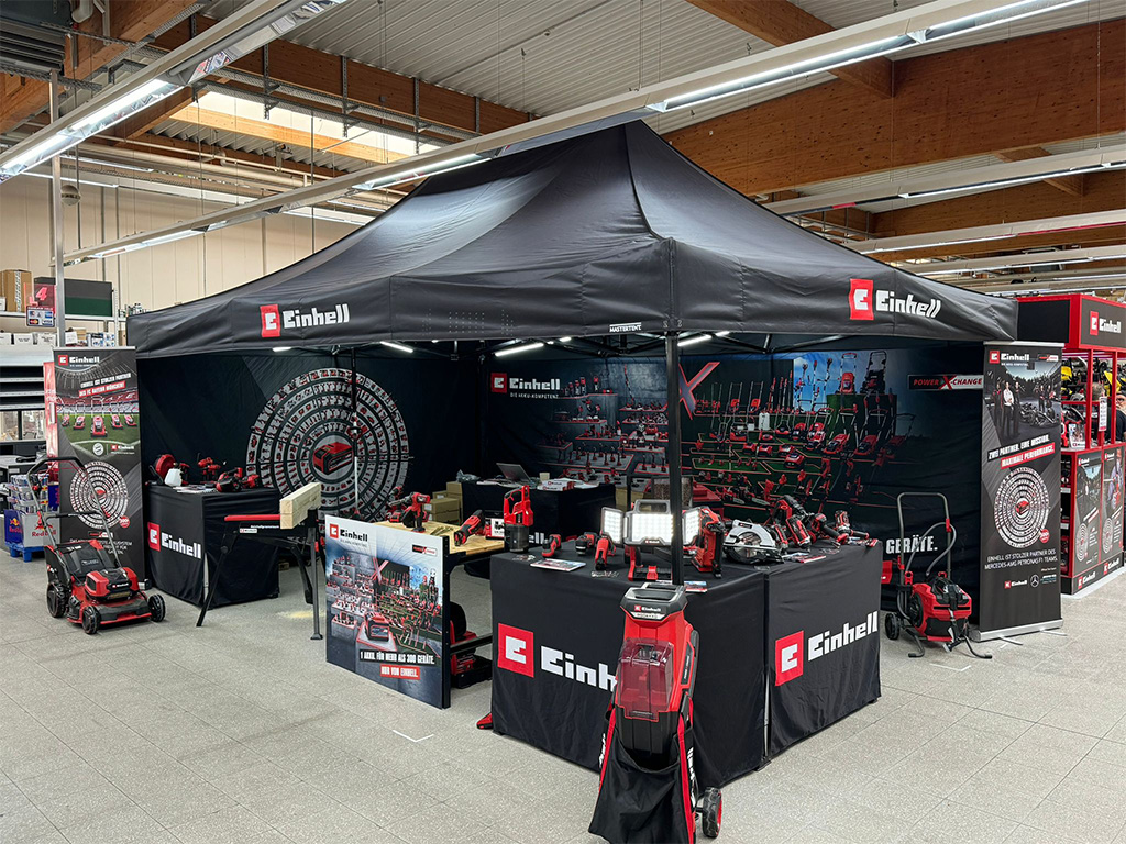 Einhell promotional setup inside a retail store with banners and various tools displayed.