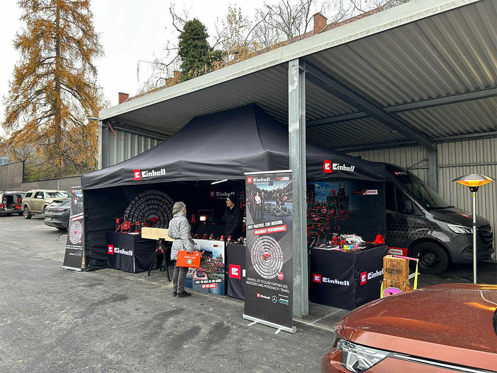 Einhell promotional tent and van set up in a parking area under a covered structure with visitors exploring.